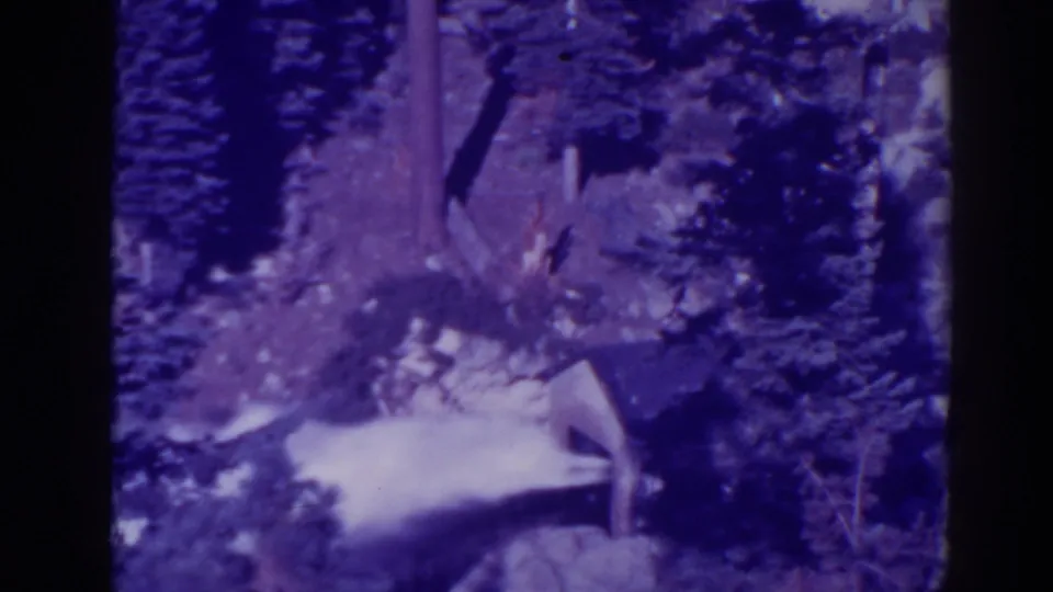 1938 Bucks Lake home-movie frame with water spraying through a rocky forest area, softened by grain and a blue-purple color cast.