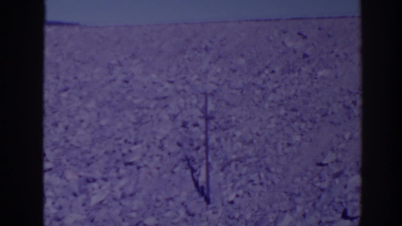 Rocky barren hillside under pale sky with a utility pole and dark film borders.