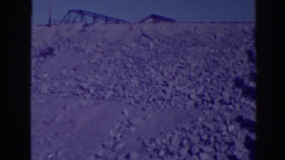 Bucks Lake area hillside in 1938, with rocky foreground, distant truss structure, utility pole, and low roofline.