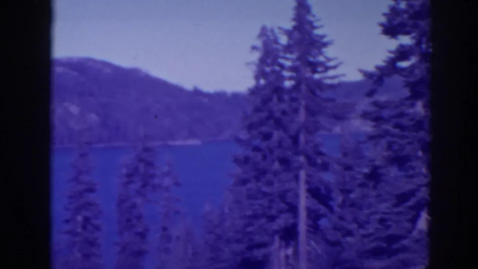 Bucks Lake landscape in 1938 8mm footage, with foreground pines, blue water, and low forested hills.