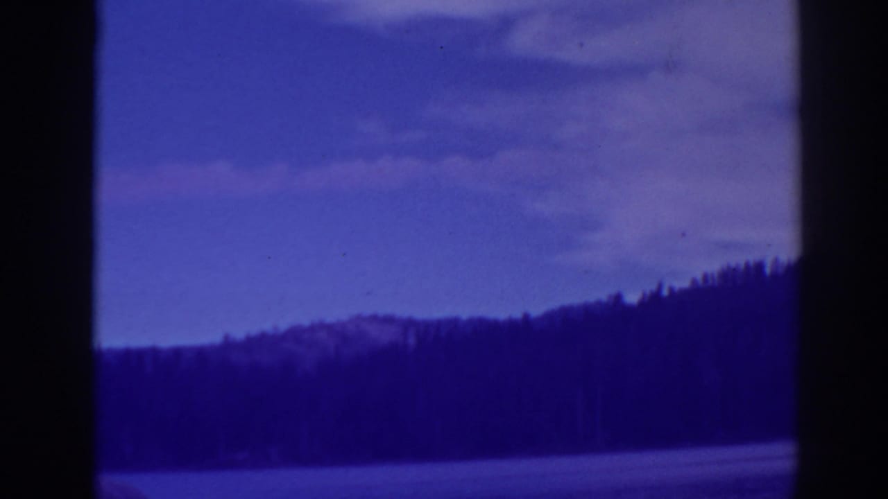 Blue-tinted lake and forested shoreline seen through dark film-frame borders.