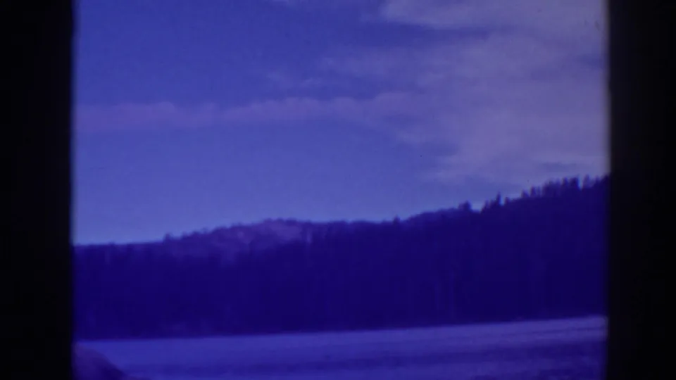 Blue-shifted 1938 home-movie frame of Bucks Lake with forested shore, low hills, and open water.