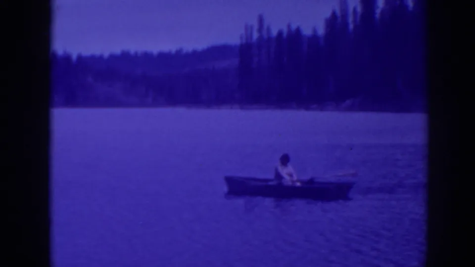 At Bucks Lake in 1938, a distant person sits in a small rowboat on blue-tinted water near a wooded shoreline.