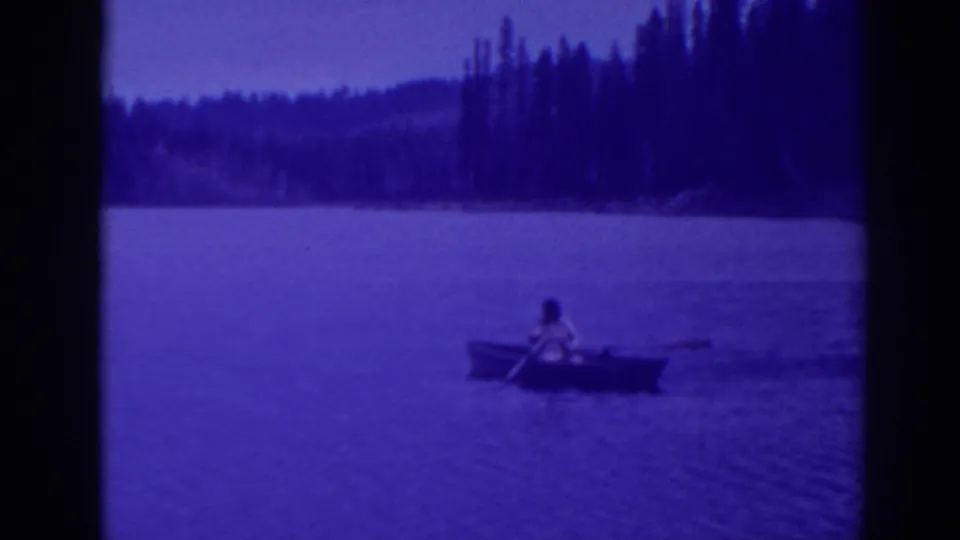 Blue-shifted 8mm frame from Bucks Lake showing a lone adult rowing away from the forested shoreline in 1938 footage.