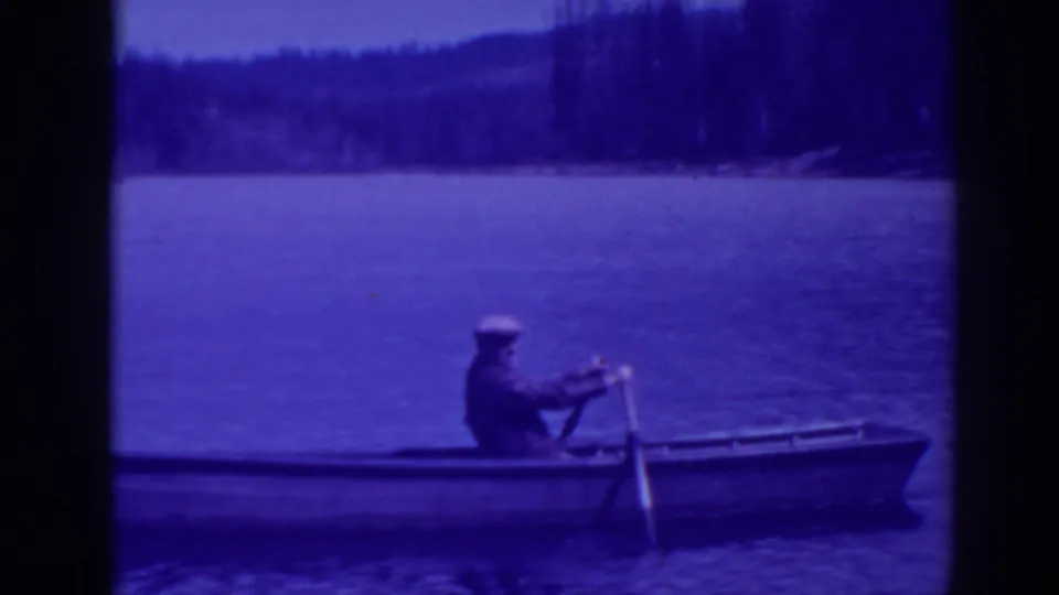 A man rows a narrow wooden boat across Bucks Lake, California, in 1938 home-movie footage with purple-tinted 8mm film color.