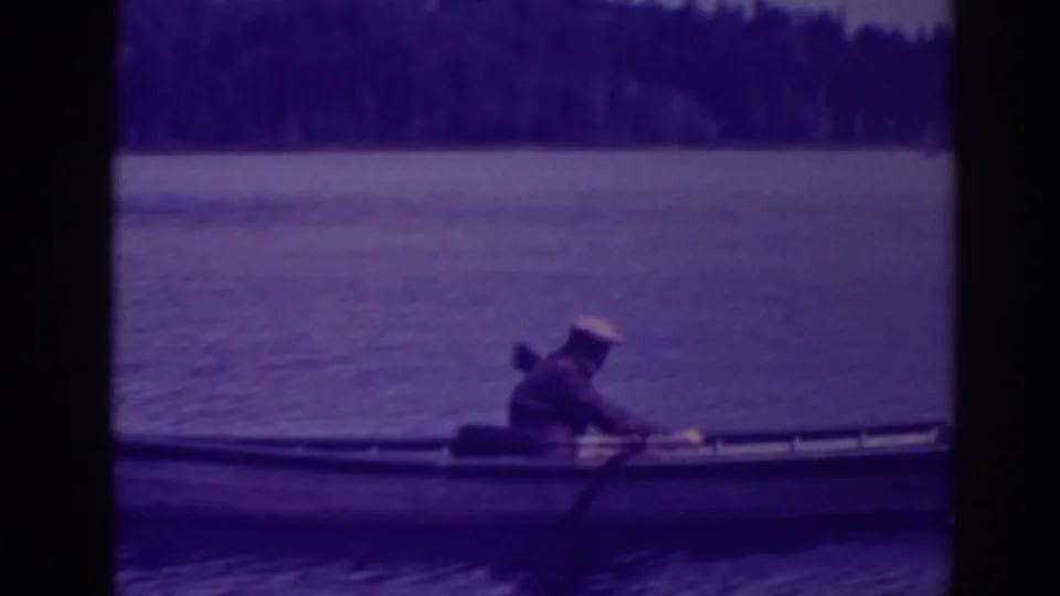 A 1938 Bucks Lake home-movie frame shows the rower leaning into a stroke, with calm water and forested shoreline behind him.