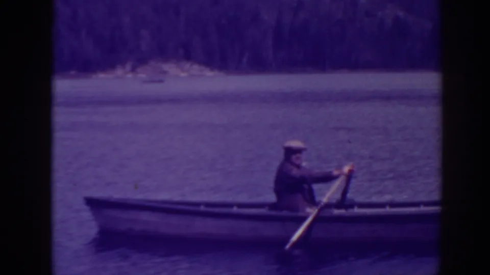At Bucks Lake, California, a man in a cap rows a small wooden boat across calm water in 1938 home-movie footage.
