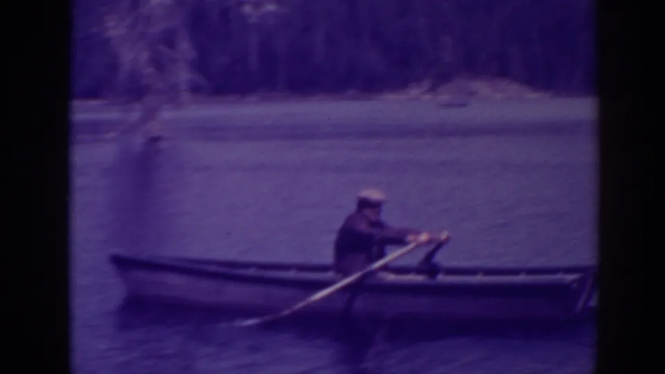 The rower leans forward with the oars in a small boat on Bucks Lake, with trees lining the background.