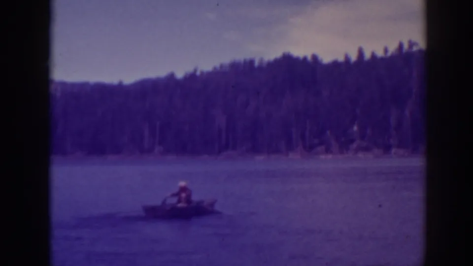 The rowboat remains distant on Bucks Lake, framed by calm water, wooded hills, and the purple cast of the 8mm scan.