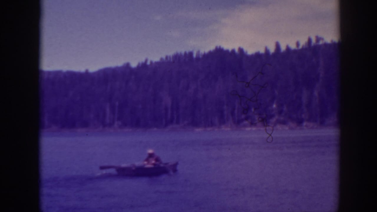 Small rowboat with a person crossing a lake below a forested hillside.