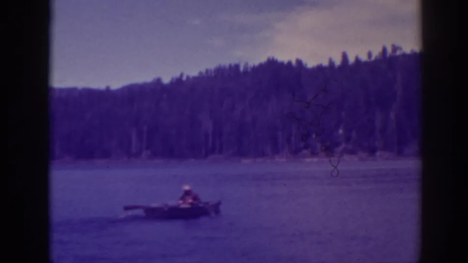 At Bucks Lake, California in the supplied 1938 metadata, a distant rower in a small boat moves across calm water below wooded hills.
