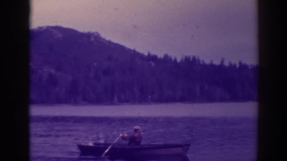 A distant rower crosses Bucks Lake in a small boat, with wooded hills and mountain shoreline behind.