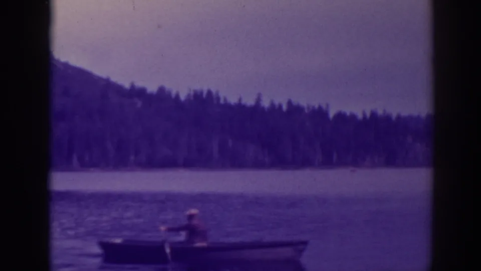 The rower remains distant on Bucks Lake, framed low against water, tree-lined shore, and hazy hills.