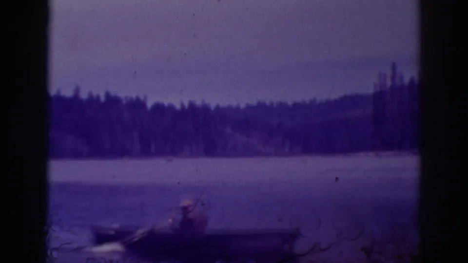 At Bucks Lake, California, a distant rower sits in a small boat near the edge of a calm, forest-lined lake.