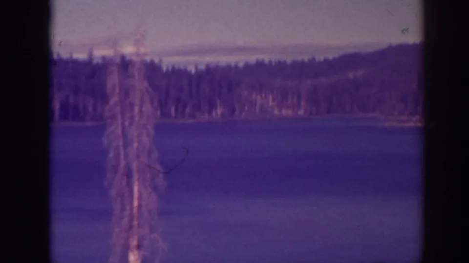 Bucks Lake, California, home-movie frame showing calm water, pine shoreline, distant hills, and 8mm gate edges.