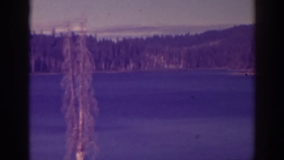 Archival 8mm view at Bucks Lake with still water, pine-covered shoreline, distant hill, and visible film gate borders.