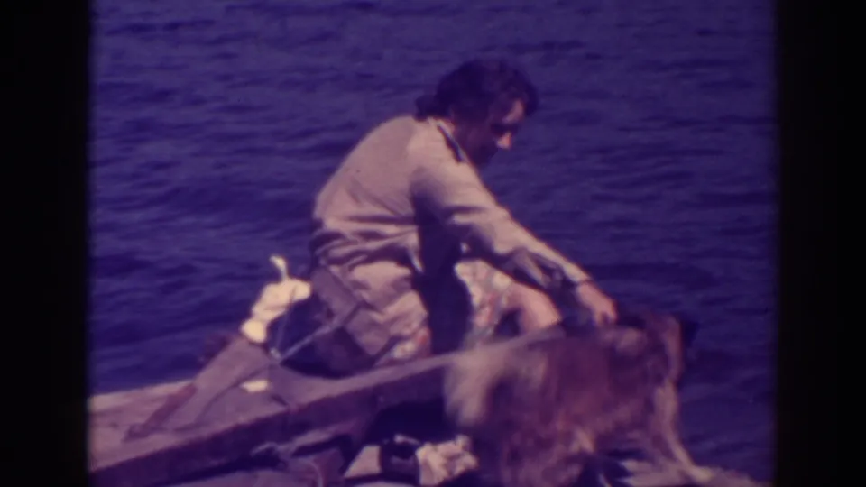 At Bucks Lake in 1938, a man sits in a wooden boat with a dog beside him on the water.