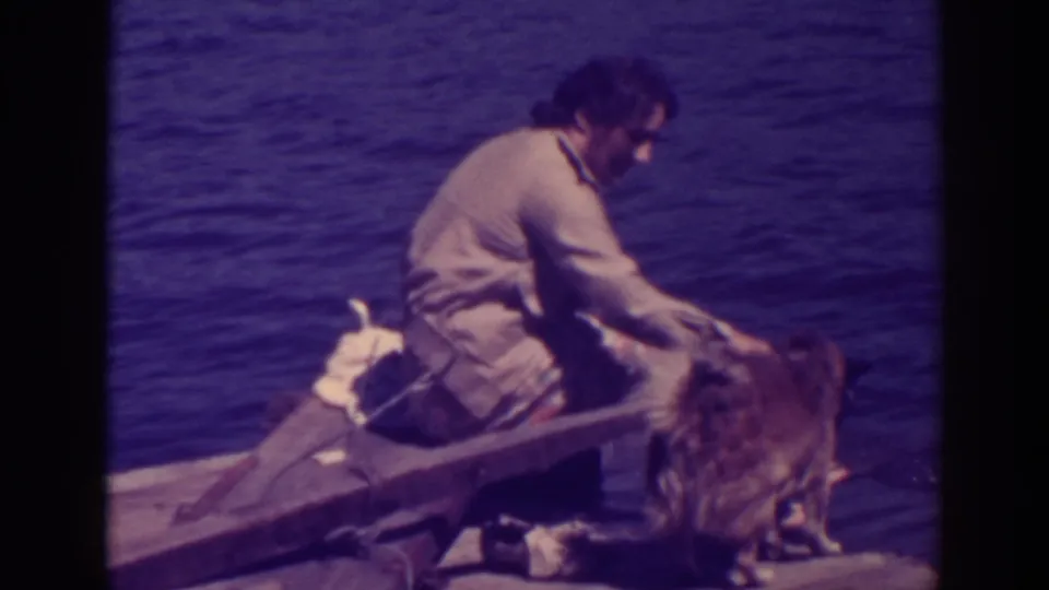 At Bucks Lake in 1938, the woman bends toward the large dog from her seat on the wooden raft, with lake water behind them.