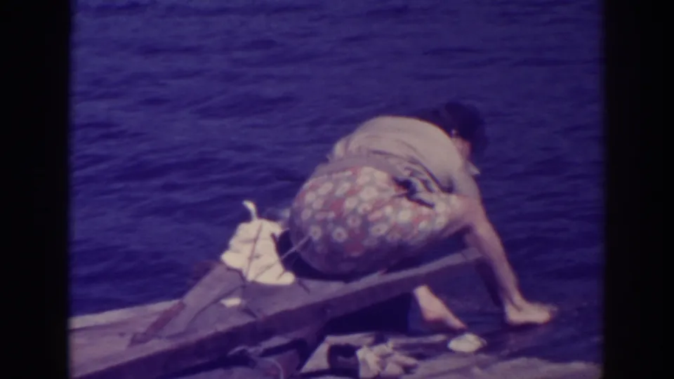 The woman leans forward from the wooden dock at Bucks Lake, reaching toward the water while washing by hand.