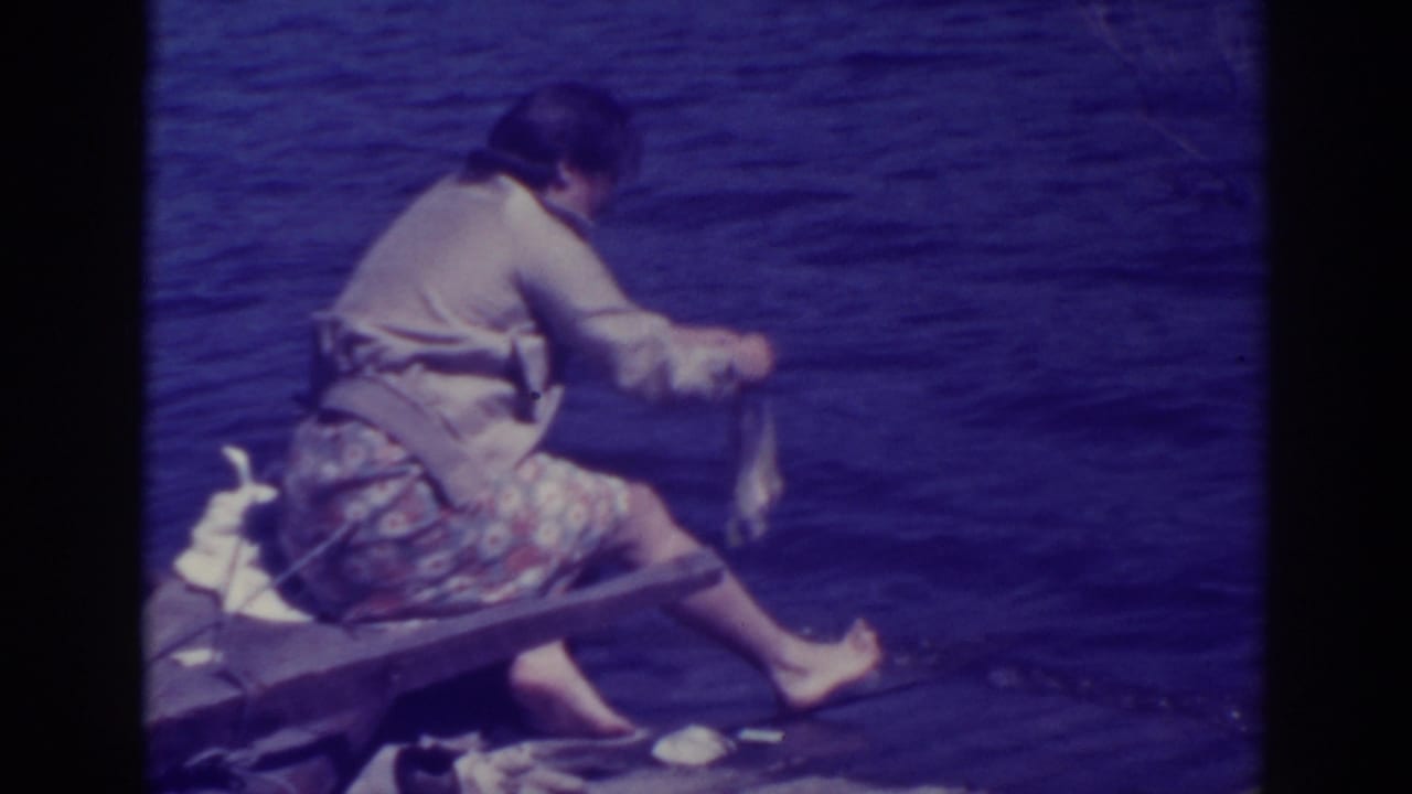 Woman seated by lake water holding cloth on a wooden bench or dock edge.