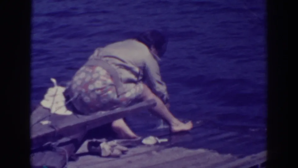 The woman leans farther over the Bucks Lake pier, barefoot, with her hand and the fish close to the rippling water.