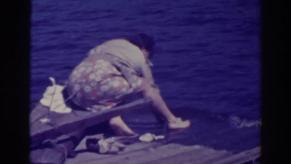 A 1938 Bucks Lake home-movie frame shows the woman crouched low on the pier, reaching down as the fish is rinsed near the lake surface.