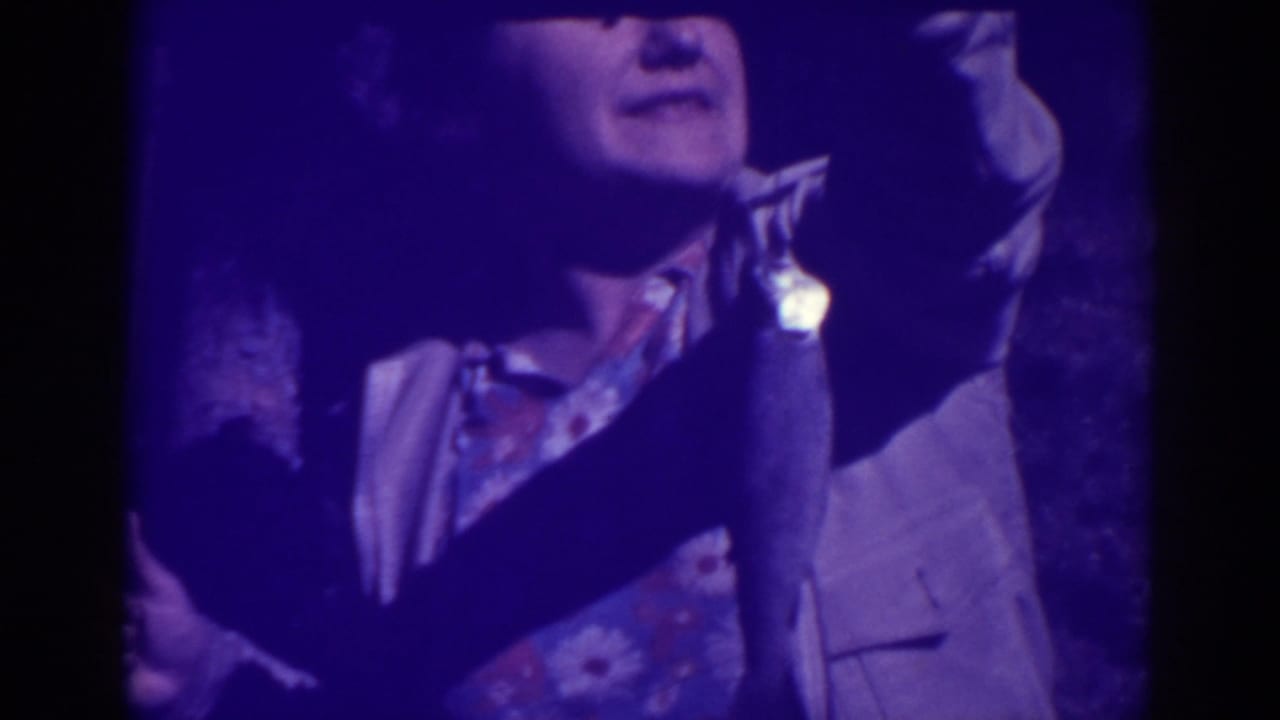 Woman holds a fishing rod and dangling fish in dim purple-tinted home-movie footage.