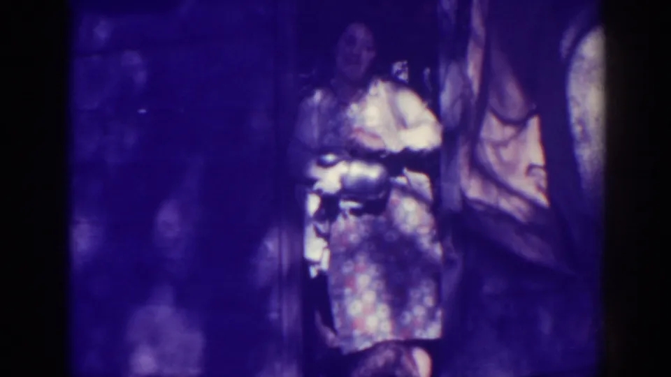 In the Bucks Lake home-movie scene, the woman looks down toward the kettle while standing partly in shadow near the doorway.