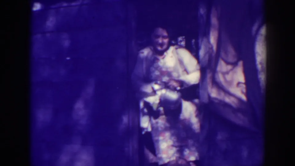 The woman bends slightly over the kettle in the doorway, with the 1938 Bucks Lake frame showing heavy purple cast and grain.