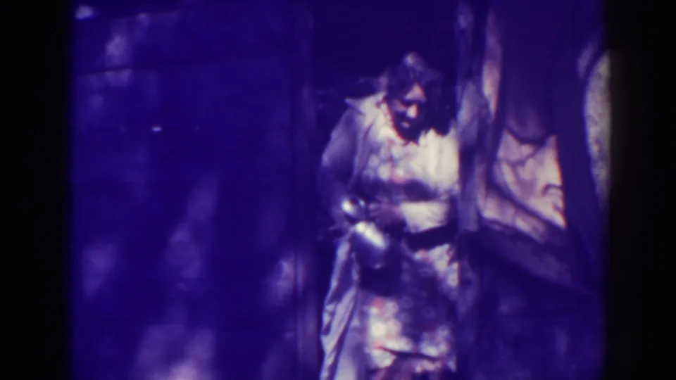 1938 Bucks Lake home-movie frame showing a person in dim purple light handling gear in an interior or sheltered setting.