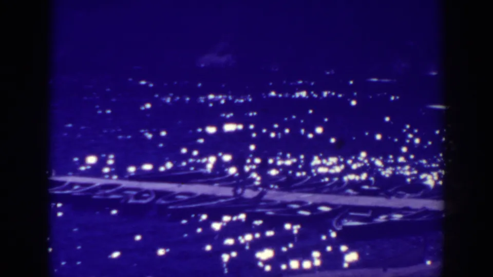 Bucks Lake night view on 8mm film, with bright shoreline lights, dark water, and heavy blue-purple color shift.