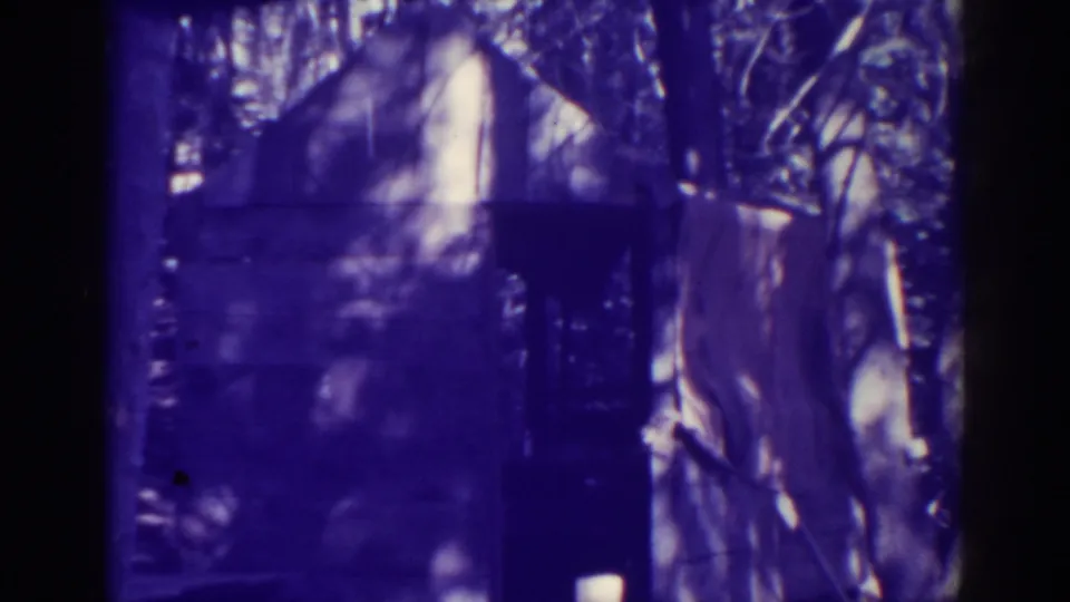 Grainy 1938 Bucks Lake frame with a small structure, surrounding trees, and strong gate shadow from the 8mm scan.