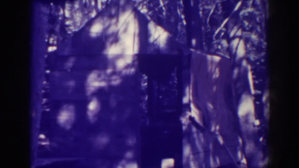 Final 8mm still from Bucks Lake showing the shed area under mottled sunlight, with no clearly identifiable person visible.