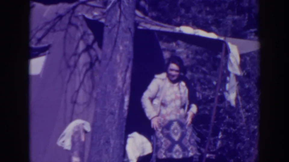 An adult in patterned clothing stands at the Bucks Lake tent entrance with laundry or cloth visible around the campsite.