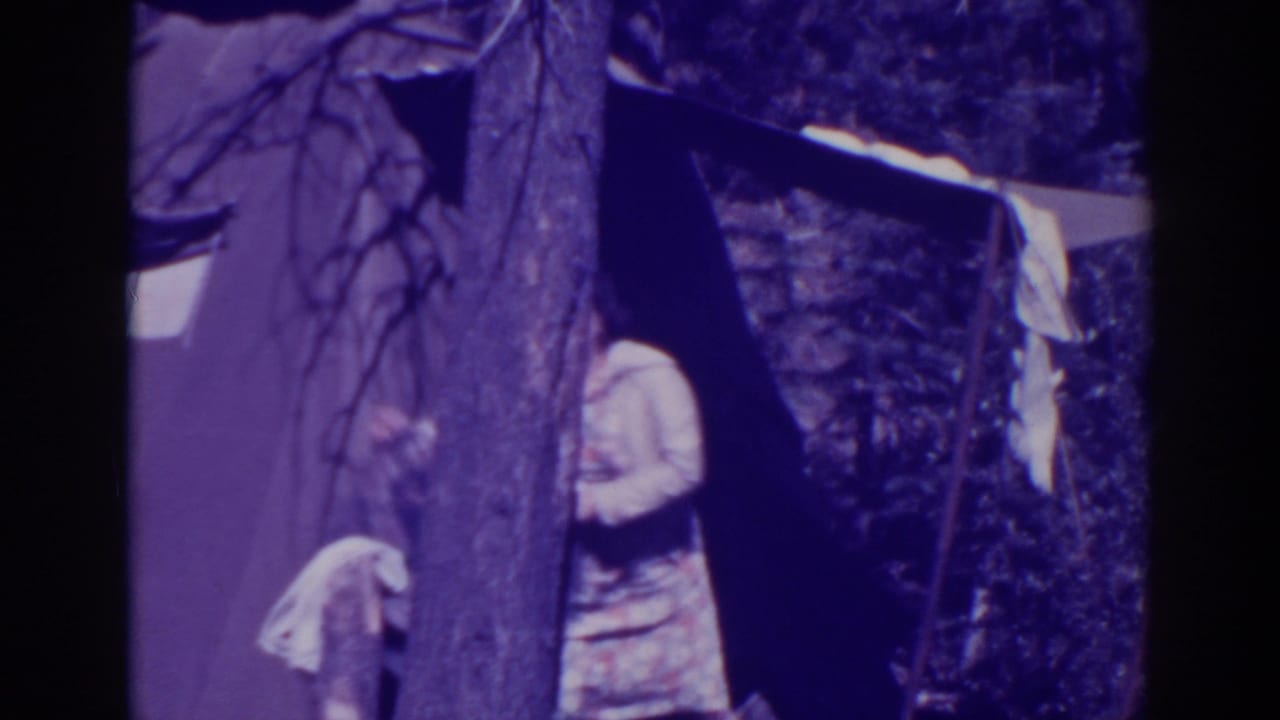 At a Bucks Lake campsite in 1938, a woman stands partly obscured beside a tree and tent while cloth hangs near the shelter.