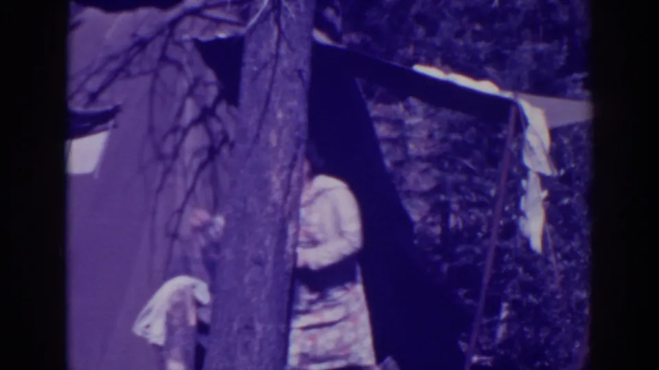 At a Bucks Lake campsite in 1938, a woman stands partly obscured beside a tree and tent while cloth hangs near the shelter.