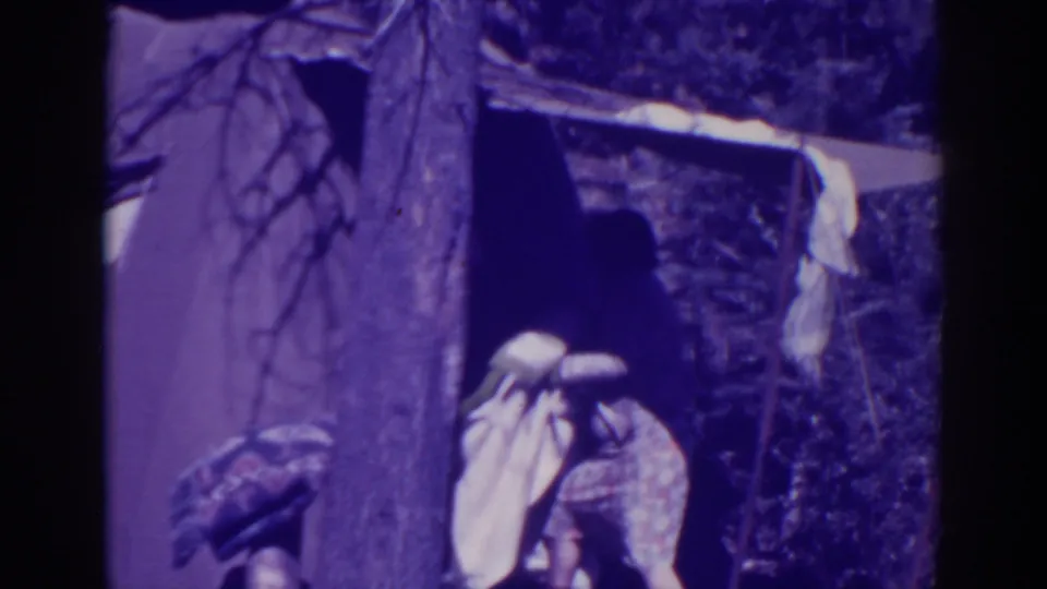 At Bucks Lake in 1938, a person stands near a canvas tent and tree while handling a light blanket or cloth.