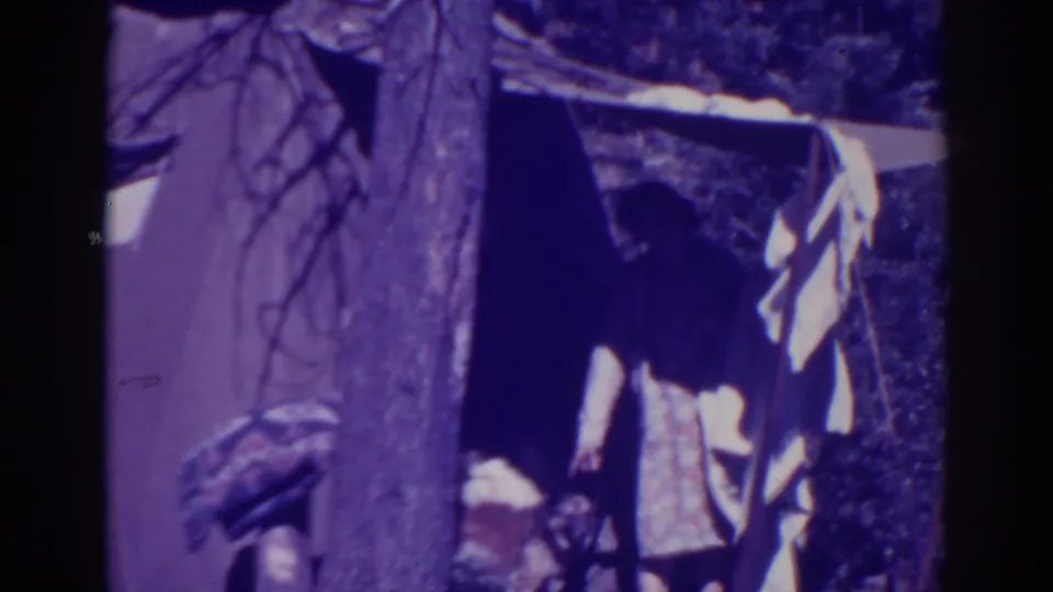 The woman stands in partial shadow at the canvas tent entrance, with a tree trunk and pale cloth visible nearby.