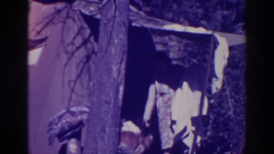 Bucks Lake 1938 home-movie frame showing a canvas tent area, tree trunk, and a partly visible seated woman at camp.