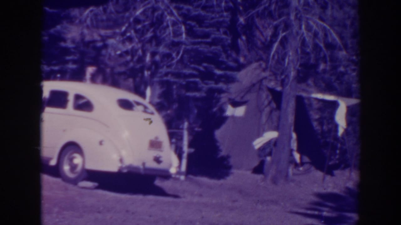 White rounded sedan parked near trees and a campsite.