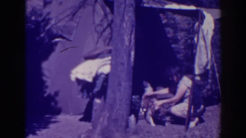 Bucks Lake 1938 home-movie frame showing a woman seated near her dog beside a tree and canvas tent.