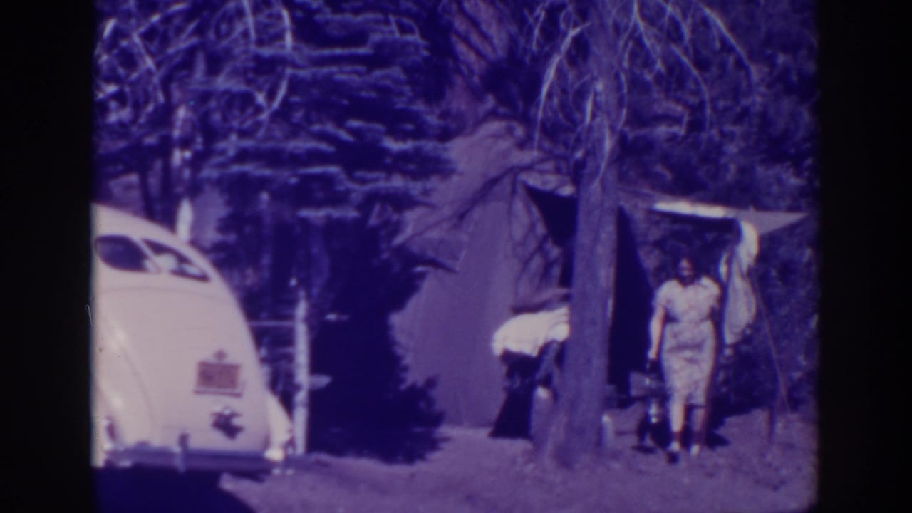 At Bucks Lake, California in 1938, a woman in a light dress stands by a canvas tent while a white rounded car sits beside trees.