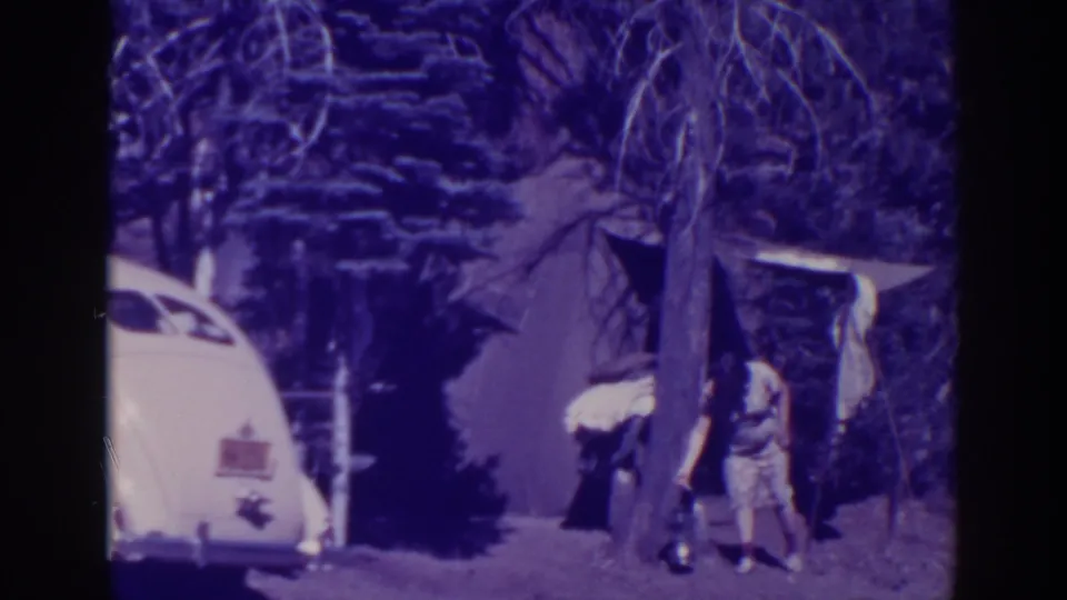 At the 1938 Bucks Lake campsite, an adult bends near the tent entrance while the white car remains parked at the left edge.