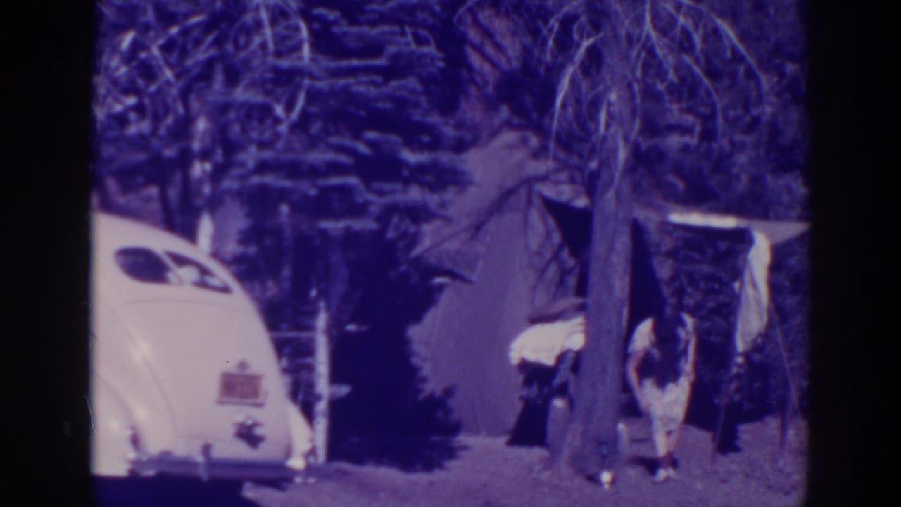 At Bucks Lake in 1938, a woman stands near a tent entrance beside a rounded white car in a shaded campsite.