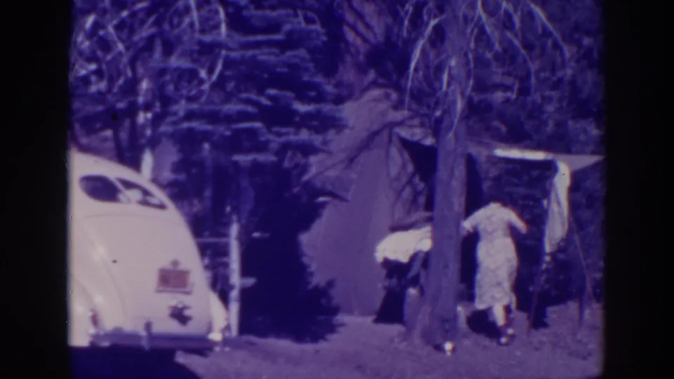 At the Bucks Lake campsite, the woman appears to bend toward objects near the tent while a white 1930s car remains parked nearby.