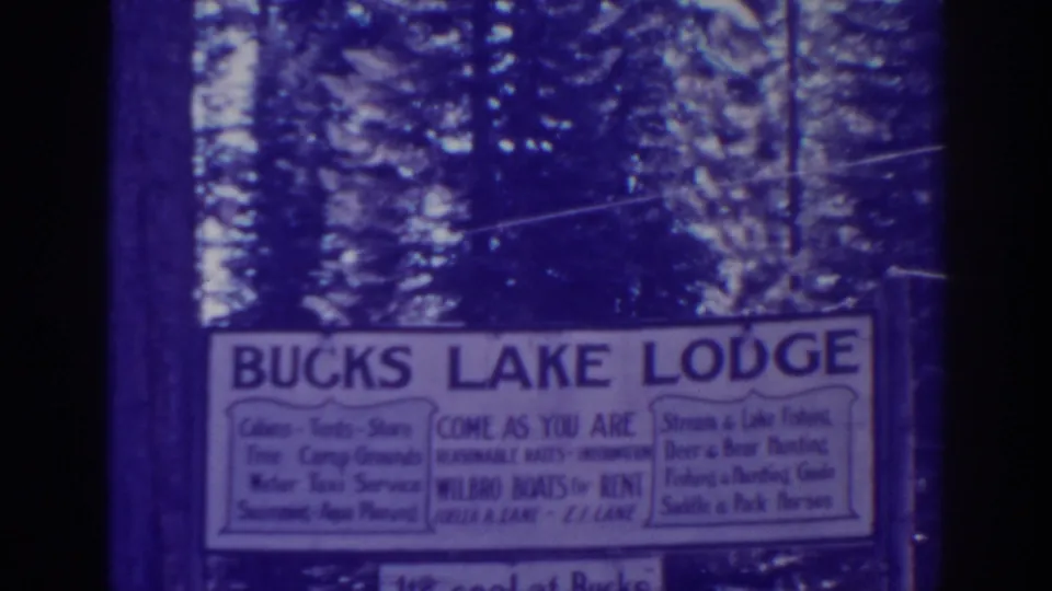 Close view of the Bucks Lake Lodge sign in a blue-purple 8mm frame, with forest visible behind it.