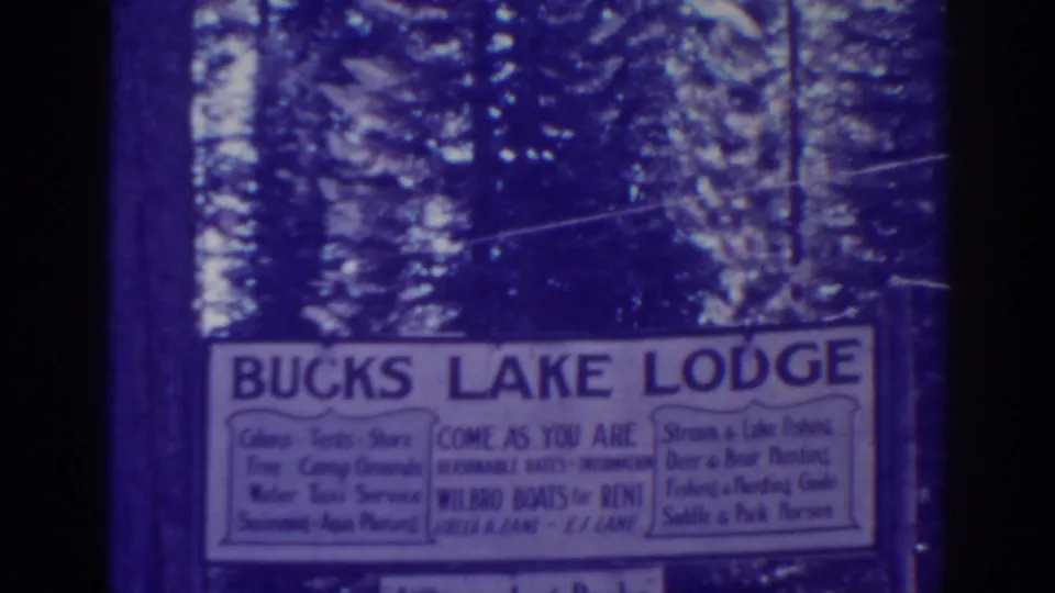 Bucks Lake Lodge sign seen close-up in vintage 8mm footage, with soft focus and wooded surroundings.