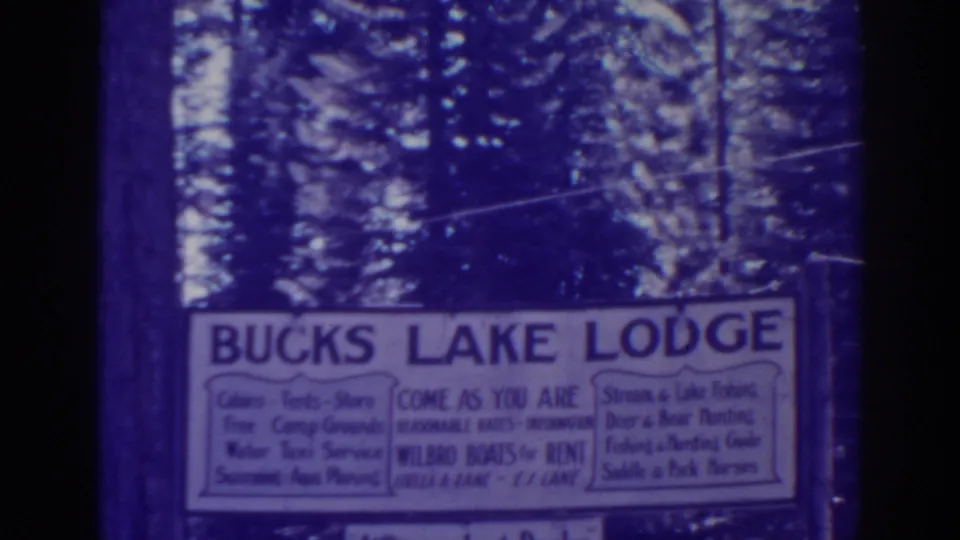 Final frame of the Bucks Lake Lodge sign, showing blue lettering, amenity panels, and pine trees behind it.