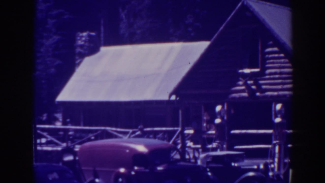 Rustic Bucks Lake lodge building with a steep roof, porch railing, pine backdrop, and parked late-1930s automobiles.