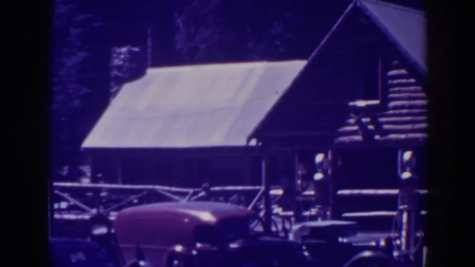 Rustic Bucks Lake lodge building with a steep roof, porch railing, pine backdrop, and parked late-1930s automobiles.